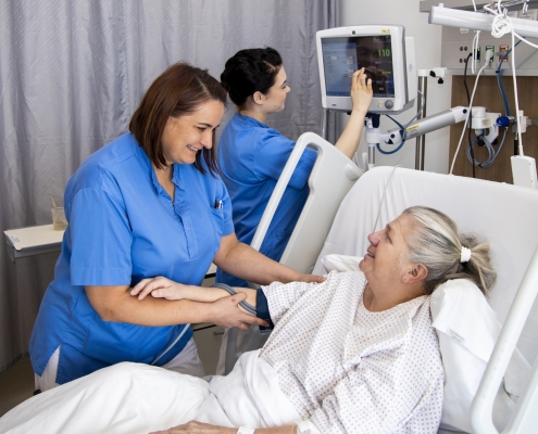 Pflegerin im Gespräch mit älteren Dame im Krankenbett